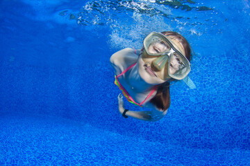 Happy young girl in snorkeling mask dive underwater in the pool.