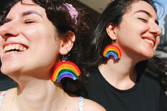 two women friends smiling with glasses wearing rainbow pride flag themed earrings *4