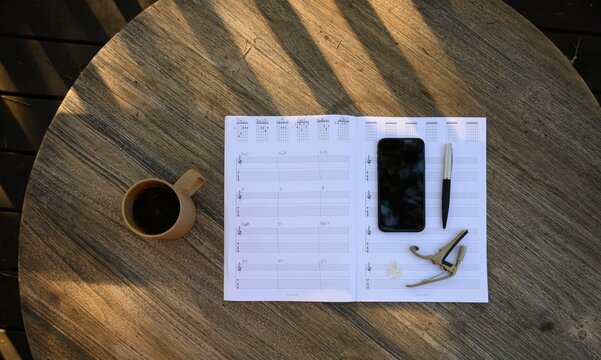 Overhead View Of Guitar Sheet Music With Phone And Coffee On Table