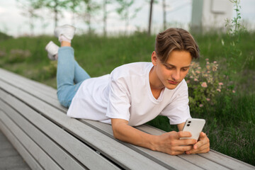 young guy lies on a bench with a mobile phone 
