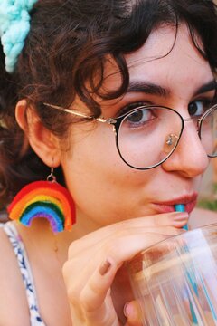 woman with rainbow earrings sipping from her ice coffee
