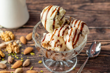 Almond, pistachio and walnut Roma ice cream in a glass bowl with caramel sauce poured over it.