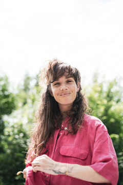 Portrait of smiling woman pink shirt cleaning glasses outside in sun
