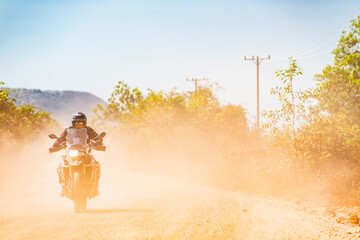 Man riding his adventure motorbike on dusty road in Cambodia
