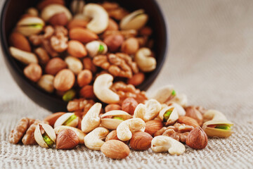 Nuts of various varieties spill out from a wooden plate on a table with a burlap cloth.