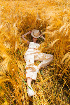 Woman with a blond hair and white hat lying in golden wheat fiel