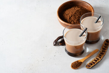 Carob drinks in glass with carob beans and powder
