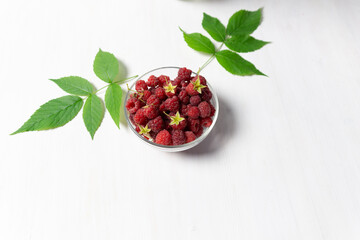 bowl of red fresh raspberries on white wooden background