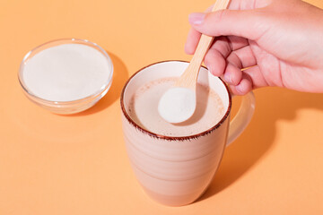 Woman adding collagen powder to coffee on colorful background