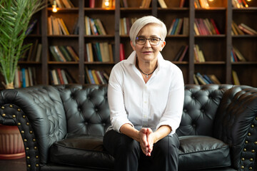 stylish adult woman in glasses in a chair on the background of books 