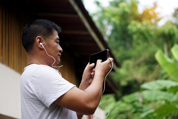  Side view of Asian man holds blank screen smartphone for text and listen to music. Concept : Wireless technology smart device internet using in daily life. Nature background.      