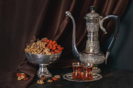 Still life with Ancient East metallic crockery - vintage jug, vase with dried fruit and plate with tea in armuda glasses
