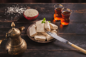 Pieces of tahini halva, sesame seeds in a bowl, tea in Turkish armudas, an vintage jug, knife with decoration