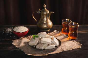 Pieces of tahini halva, sesame seeds in a bowl, tea in Turkish armudas, an vintage jug.