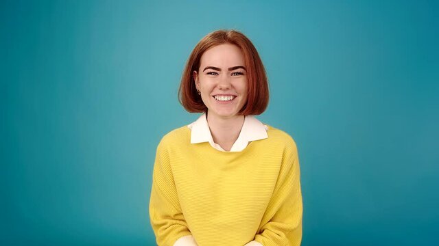 Shy actress with red hair in yellow pullover looks straight and talks with smile standing on blue at audition slow motion close view
