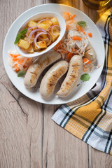 Above view of pan fried weisswurst with potato salad and sauerkraut on a white plate, vertical shot on a brown wooden background