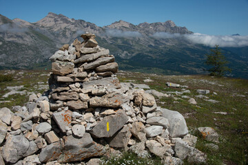 pile of stones or cairn , in the French alps with mountain tops and clouds in distance.