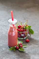 Cherry oatmeal smoothie in a glass bottle with a straw on a dark gray background