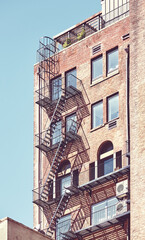 Fototapeta na wymiar Old brick building with fire escape in New York City, color toning applied, USA.