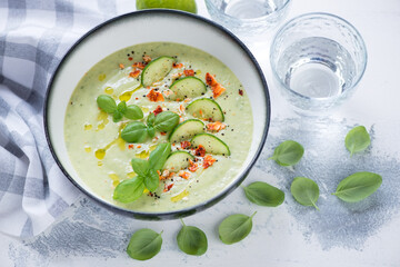 Bowl of cucumber and green basil cold gazpacho soup, horizontal shot on a white concrete background