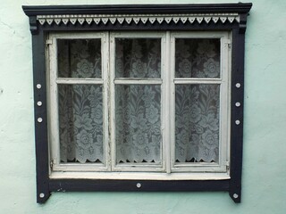 An old window with a wooden frame and white tulle curtains.