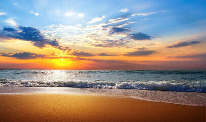 Beautiful natural seascape with colorful sunset sky. Waves of sea surf and golden sand of beach in rays of sunlight.