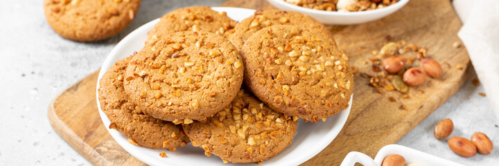 Healthy homemade oatmeal cookies with peanuts in a white plate on a light gray kitchen table closeup. Banner