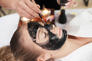 Professional Asian Thai Massage therapist woman is applying black facial mask for young caucasian female and treatment skincareat alternative medicine healing spa Center in Thailand