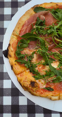 Prosciuto e arugula pizza on black and white squares background