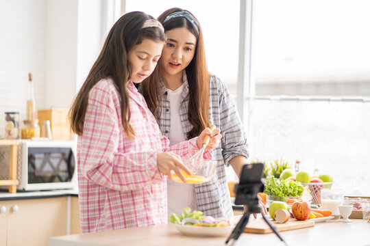 Mixed race girl younger and older sister talk and smile while play and using smartphone inside of the kitchen in the morning while eat breakfast. Family relationship mobile high speed internet network