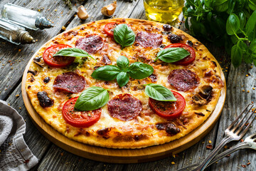 Circle pepperoni pizza with mozzarella, salami and tomatoes on wooden table