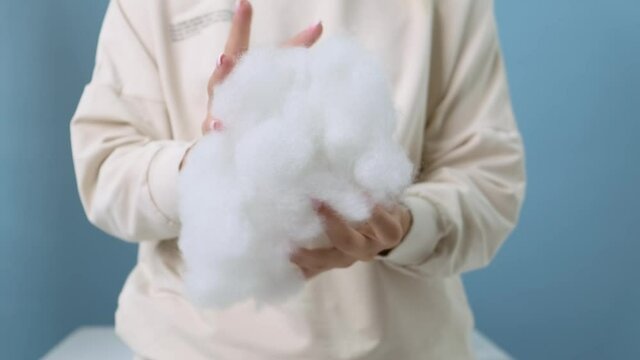 Close-up. A girl in a vanilla-colored hoodie on a blue background crumples a voluminous synthetic filler of white color