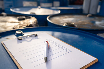 A pen on the safety checklist blank form which is placed on the chemical drum at storage area in factory. Safety in industrial concept photo. Close-up and selective focus on pen's part. - obrazy, fototapety, plakaty