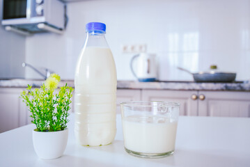 a bottle of milk and a full glass cup on the kitchen table in the background of the cozy light kitchen wall.