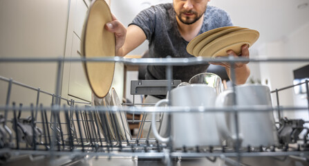The man takes the washed dishes from the dishwasher.