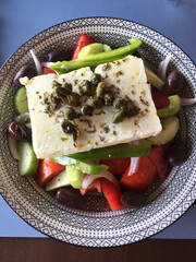 A Greek salad or horiatiki salad served in Athens and containing tomatoes, cucumbers, onion, bell pepper, caper berries, olives, feta cheese and dressed with salt, pepper, Greek oregano, and olive oil