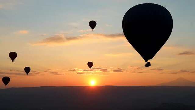 Hot air balloons at sunrise flying over the valleys in Goreme, Turkey. Red and yellow shades of the rising sun of Cappadocia. Dark silhouettes of balloons. Hot air balloon travel