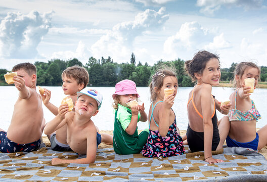 Children sit by the river and eat ice cream. - Powered by Adobe