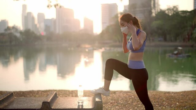 A woman exercise and take off your mask to drink water beside a pond in the city park (side view, MLS)