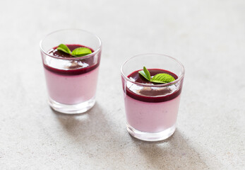 Creamy berry dessert, Panna Cotta black currant with sauce in a glass on a light background