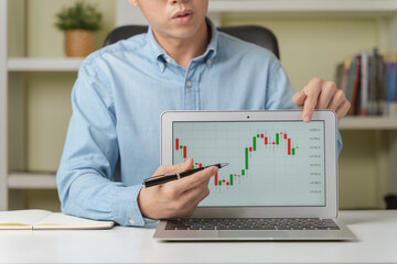 Young businessman or investor pointing on stock tickers or Cryptocurrency trading graphs to teach about investing new stock trading, Cryptocurrency as Bitcoin platform at home. Young investor concept