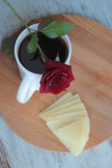 There is a coffee mug and a red rose on a round wooden stand.