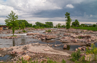 Sioux Falls, SD, USA - June 2, 2008: Heavy gray cloudscape over the green park with the rapids,...