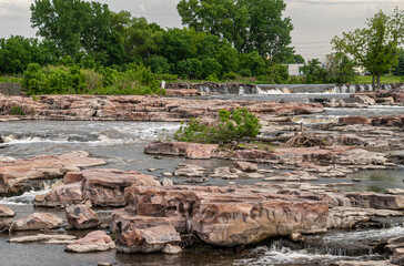 Sioux Falls, SD, USA - June 2, 2008: Focus on the cascade of waterfalls over beige rocks with some green foliage in back .