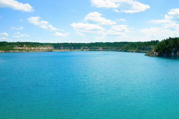 Fototapeta premium A clear blue lake under a blue sky, surrounded by rocks with a forest. Serene water surface
