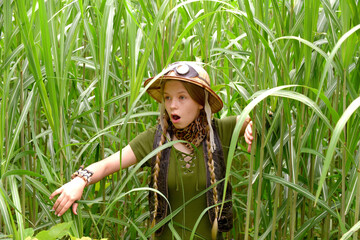 A young girl is dressed up as an explorer. She 
is seen in a tropical jungle environment Her 
face...