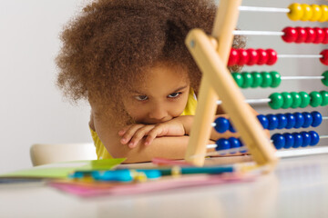 A black girl is puzzled by an example of arithmetic that she must count on the abacus