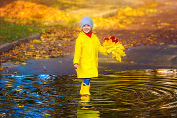 a happy girl child in a yellow raincoat and rubber boots in a puddle on an autumn walk