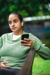 Hispanic young man with cell phone in hand and sitting in the park