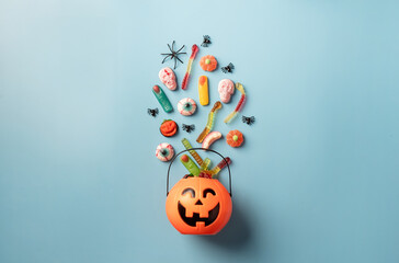Various halloween sweets and candies in a pumpkin pot top view on blue solid background